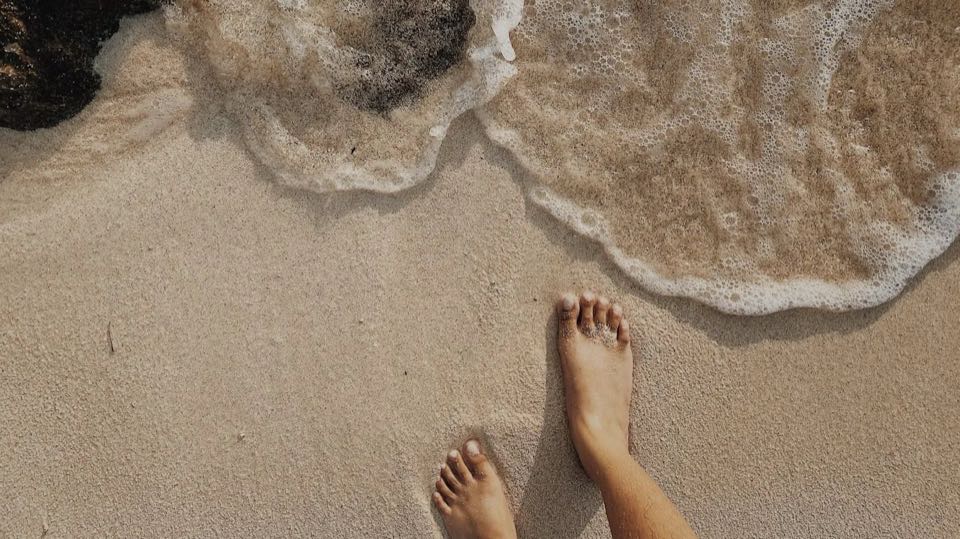 Pies descalzos en la arena de la playa junto a la orilla. La foto es ilustrativa.